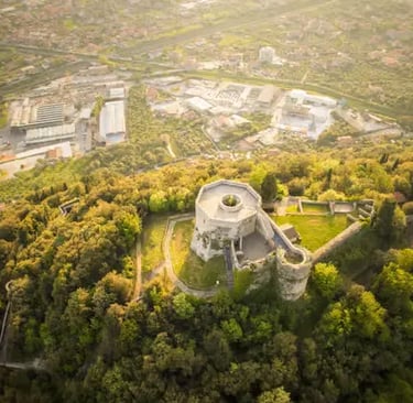 Drone shot of medieval castle ruins surrounded by green forest and urban sprawl