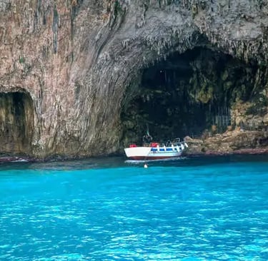 Tour boat anchored inside limestone sea cave with turquoise water on Salento coast near Otranto