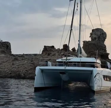 Luxury catamaran anchored beside dramatic limestone cliffs at sunset Menorca