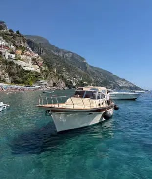 Traditional Gozzo tour boat anchored in turquoise water off Positano coastline