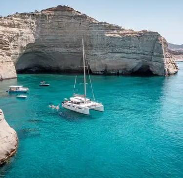 White catamaran anchored in turquoise water beside white volcanic cliffs of Kleftiko Milos