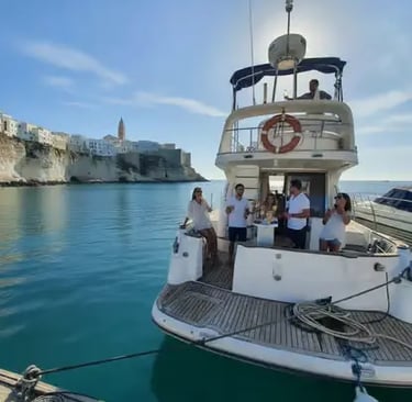 Yacht crew and guests onboard luxury boat with Polignano a Mare cliffside town in background