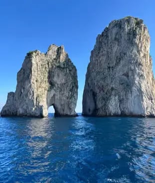 Iconic Faraglioni rocks of Capri rising from the deep blue Tyrrhenian Sea on a clear summer day.