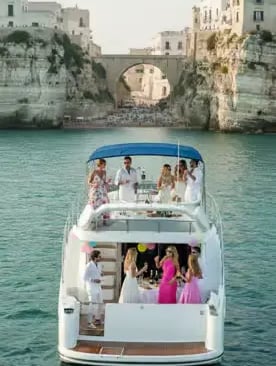 Guests enjoying Apulian aperitif party on luxury yacht beneath dramatic Polignano a Mare cliffs