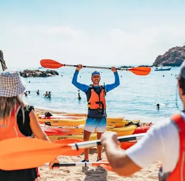 Certified sea kayak instructor holding paddle on Tossa de Mar beach with group and kayaks