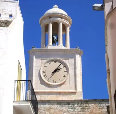  White limestone clock tower in historic center of Locorotondo against clear blue Puglia sky