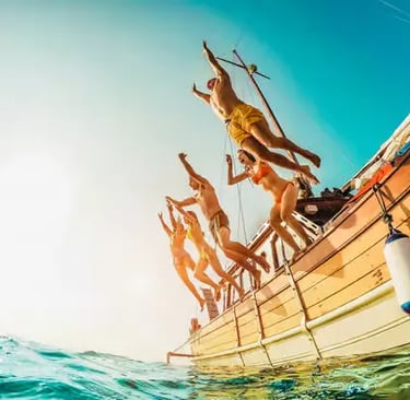 Group of guests jumping from a traditional wooden boat into turquoise Mediterranean sea water