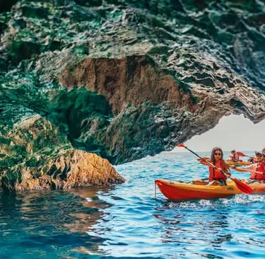 Kayakers in red life jackets paddling through a sea cave into turquoise Costa Brava water