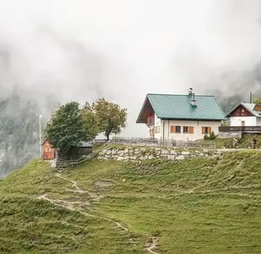 A beautiful white alpine mountain house with a green roof nestled on a grassy slope of the Nordkette mountains 