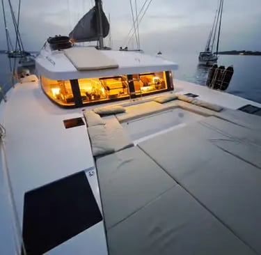 Luxury catamaran foredeck with cushions and warm cabin lights at dusk in Menorca