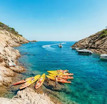 Colorful sea kayaks resting on a rocky shore inside a crystal clear Costa Brava cove