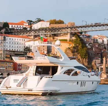 Private luxury yacht with Portuguese flag on Douro River beneath iconic Porto iron bridge.