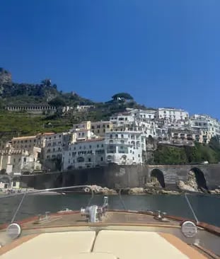View of Amalfi town white buildings on hillside from the bow of a Gozzo boat on a sunny day
