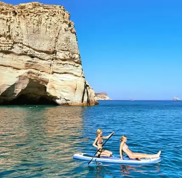 Two women paddleboarding near white Kleftiko cliffs on turquoise water in Milos