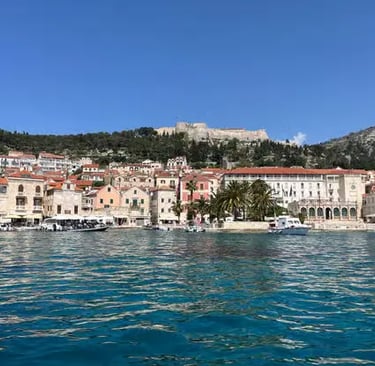 Hvar Town harbor with stone houses, palm tree and Spanish Fortress on hilltop above