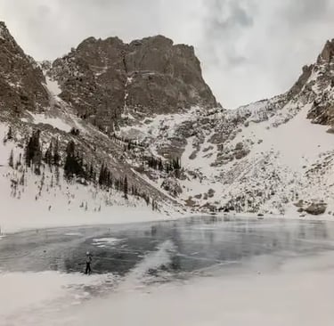 Wide view of a frozen alpine lake surrounded by dramatic snowy mountain cliffs.