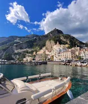  Traditional Gozzo boat moored in Amalfi harbor with colorful town and cliffs in background
