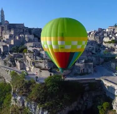 Green and yellow hot air balloon floating above the ancient Sassi di Matera stone houses and canyon