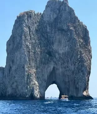 Small boat passing through the natural arch of the Faraglioni rocks on Capri private boat tour.