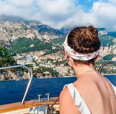 Woman on a Gozzo boat deck gazing at the Positano cliffside village from the sea