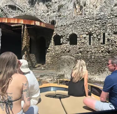 Guests on small boat approaching hidden stone sea cave along Golfo del Pecoriello in Capri