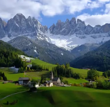 The Dolomites in spring — snow-crowned peaks rising above emerald meadows and quiet alpine villages