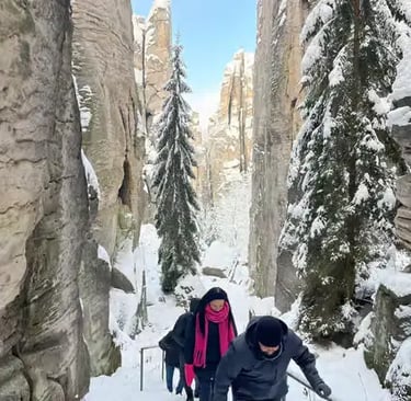 Two hikers walking between snow-covered sandstone cliffs in Bohemian Paradise