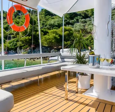 Teak deck lounge seating area on a Gulet with turquoise water and green coastline