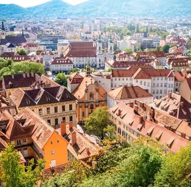 Wide panoramic view of Graz city rooftops and surrounding mountains from Schlossberg.
