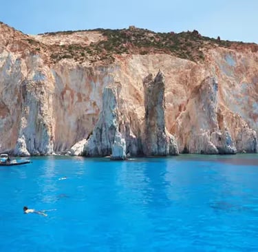 Kleftiko white volcanic cliffs and turquoise water in Milos Greece with swimmer and boats