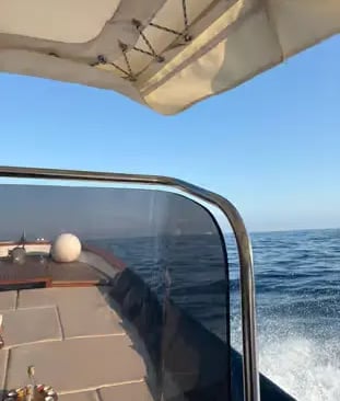 Traditional Gozzo boat with shade canopy cruising on open Mediterranean Sea along Amalfi Coast