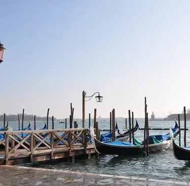Traditional Venetian gondolas docked at a pier under a clear sky near Saint Mark's Basin.