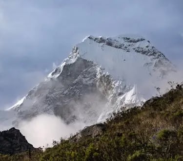 Image of Mount Kilimanjaro’s snow-capped peak surrounded by clouds, with green foothills in the fore