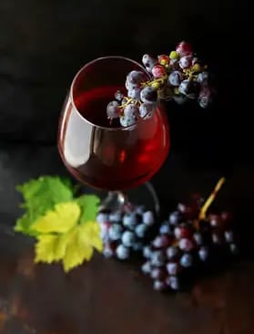 Glass of red wine with fresh dark grapes on moody dark background still life