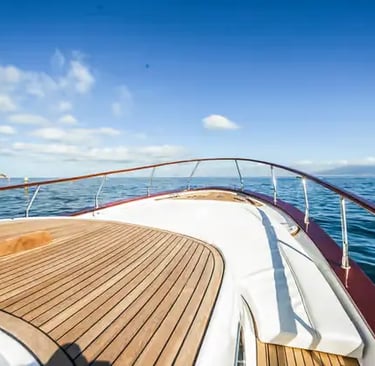 Teak deck bow of a Gozzo boat cruising toward the Amalfi coastline under blue sky