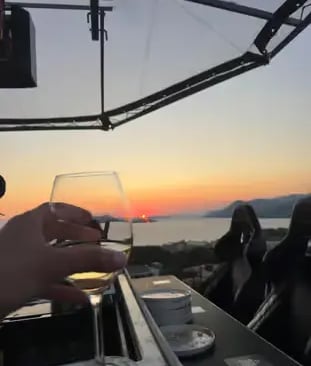 Guest holding wine glass at sunset on Dinner in the Sky platform above Dubrovnik coast