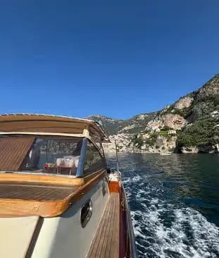 Traditional wooden Gozzo boat cruising along the Amalfi Coast cliffs on a clear day