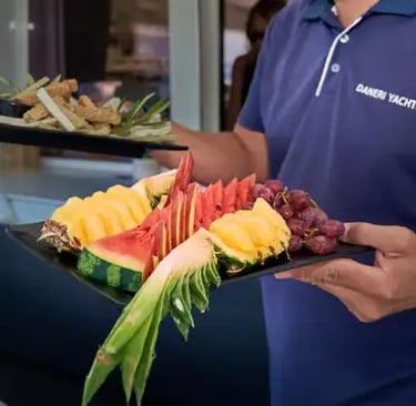 Crew serving fresh tropical fruit platter onboard Milos premium sailing tour