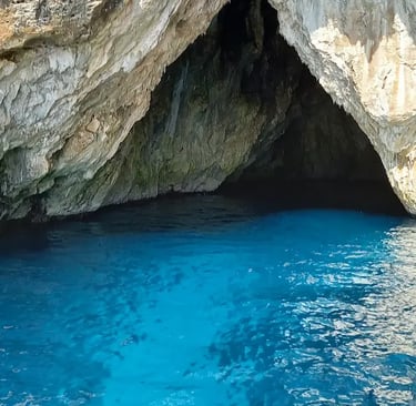 View from boat bow approaching dramatic limestone sea cave with electric blue water in Salento