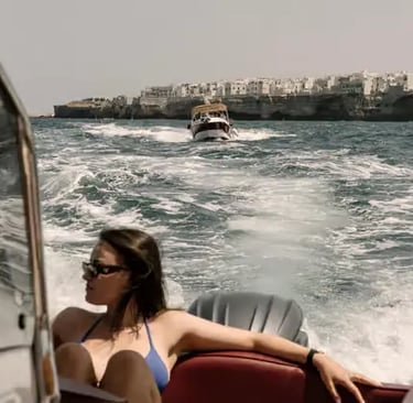 Woman in bikini lounging on speedboat cruising past whitewashed Polignano a Mare cliffs