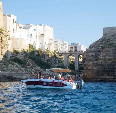 Small private boat with tourists exploring dramatic Polignano a Mare cliffs, Puglia coast.