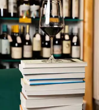 Glass of Primitivo wine on a stack of books with wine bottles in the background