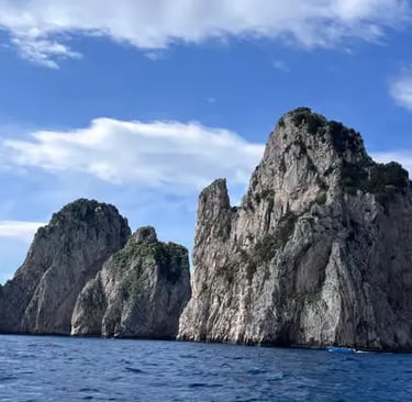 Faraglioni rock formations of Capri rising from the deep blue Tyrrhenian Sea, seen from a boat.