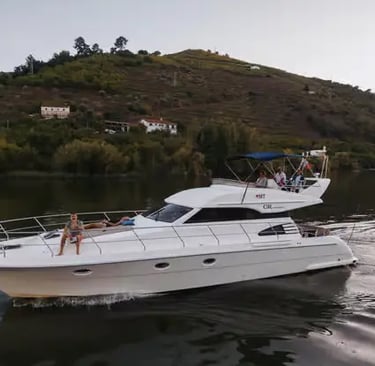 Private white motor yacht cruising calm Douro River with green vineyard hills behind