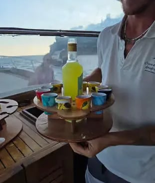 Crew member serving limoncello shots on wooden tray during Amalfi Coast boat tour