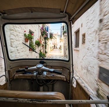 POV from inside Ape Calessino driving through narrow white-walled Puglia alley