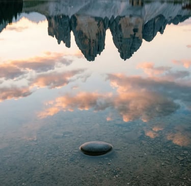 Tre Cime di Lavaredo reflected in still Alpine lake water with smooth stone