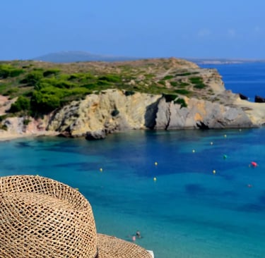 Straw hat on a ledge overlooking a turquoise beach and rocky coastline in Menorca, Spain