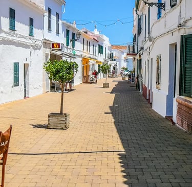 Sun-drenched whitewashed street with green shutters and string lights in Menorca, Spain