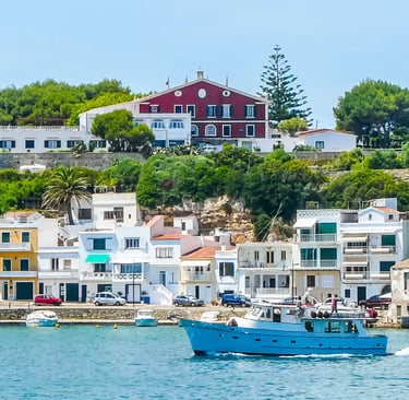 Blue fishing boat in a harbor with colorful waterfront houses in Menorca, Spain